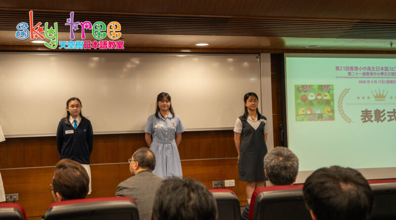 DSC05236 | 天空樹日本語教室 Three female students stand at the front of a classroom stage giving a presentation to an audience, with a projector screen showing slides on the right.