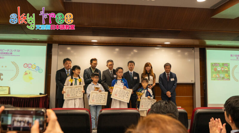 DSC05254 | 天空樹日本語教室 Children on stage receiving certificates and trophies, with adults in suits behind them and audience taking photos