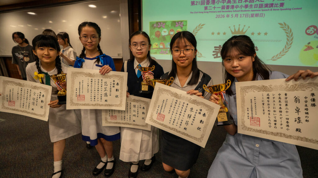 DSC05267 | 天空樹日本語教室 Group of five students in school uniforms pose with certificates and gold trophies at an award ceremony in a classroom.